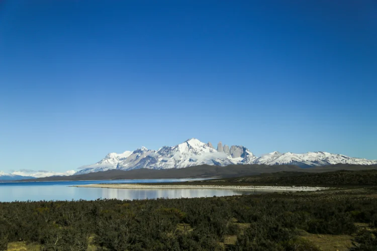 A snowy mountain in the background with flatwater in the foreground. The sky is bright blue.