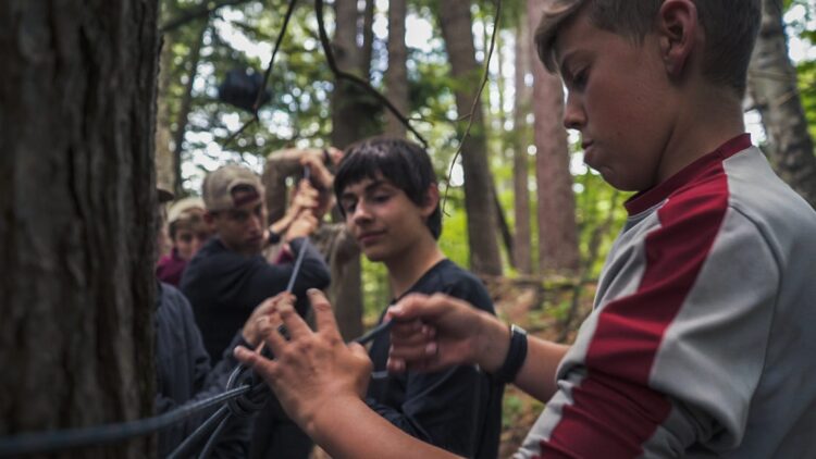 Teens working together on a rope activity in a forest during a wilderness expedition.
