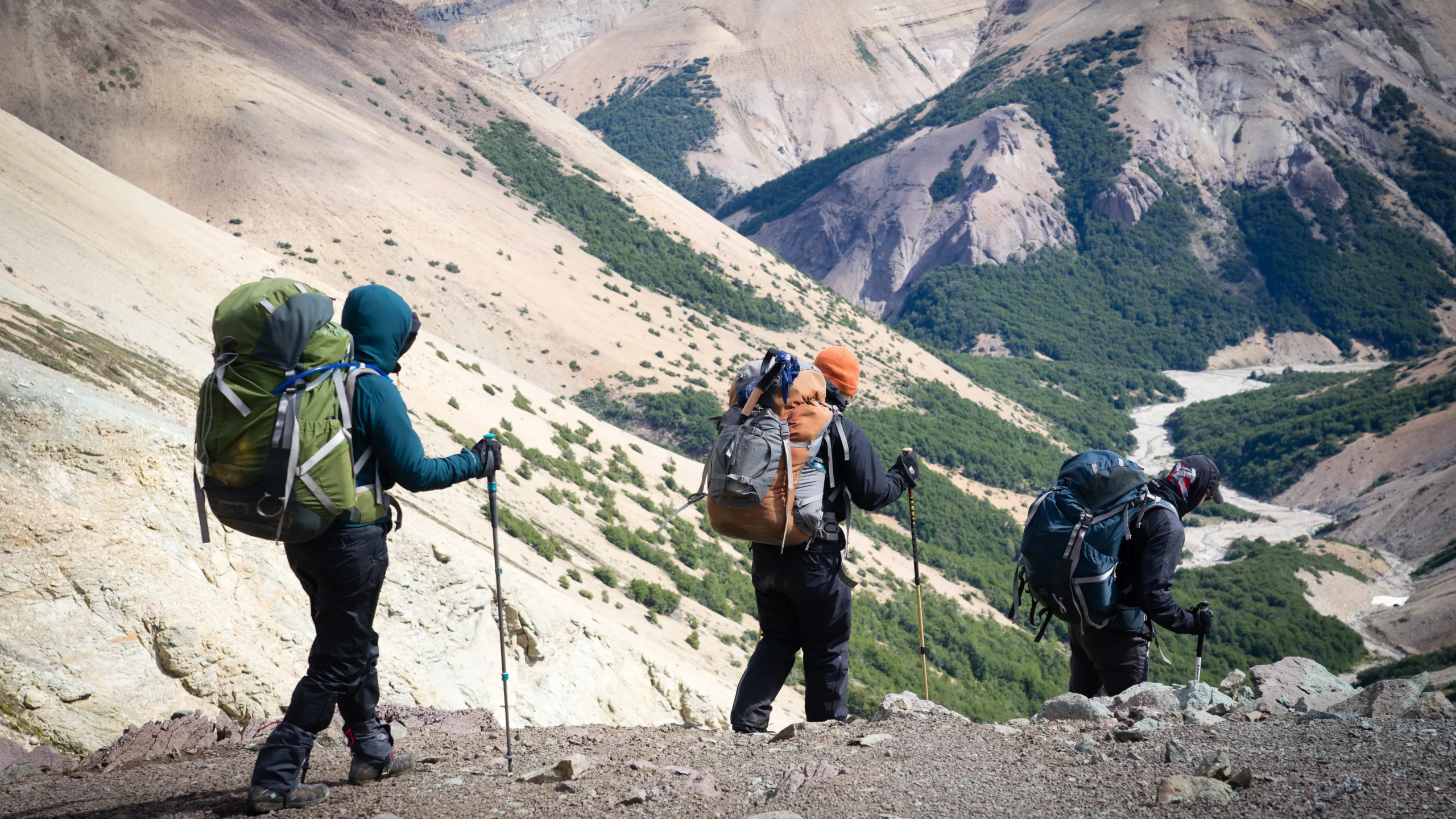 three people wearing large backpacks hike through rocky mountains