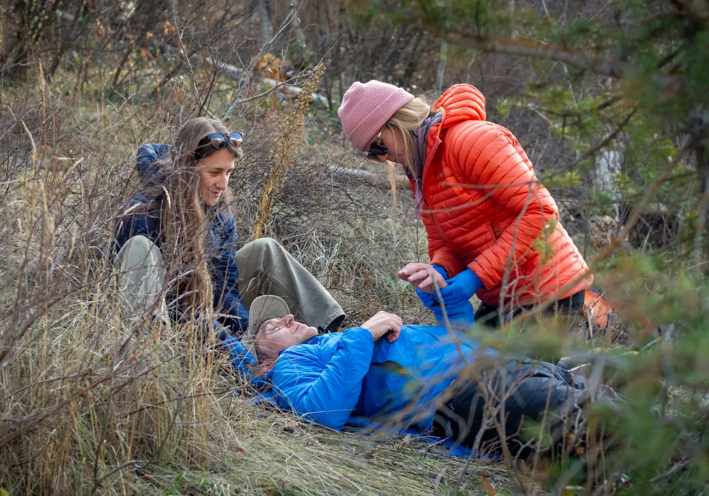 two woman in puffy jackets help a person lying on the ground