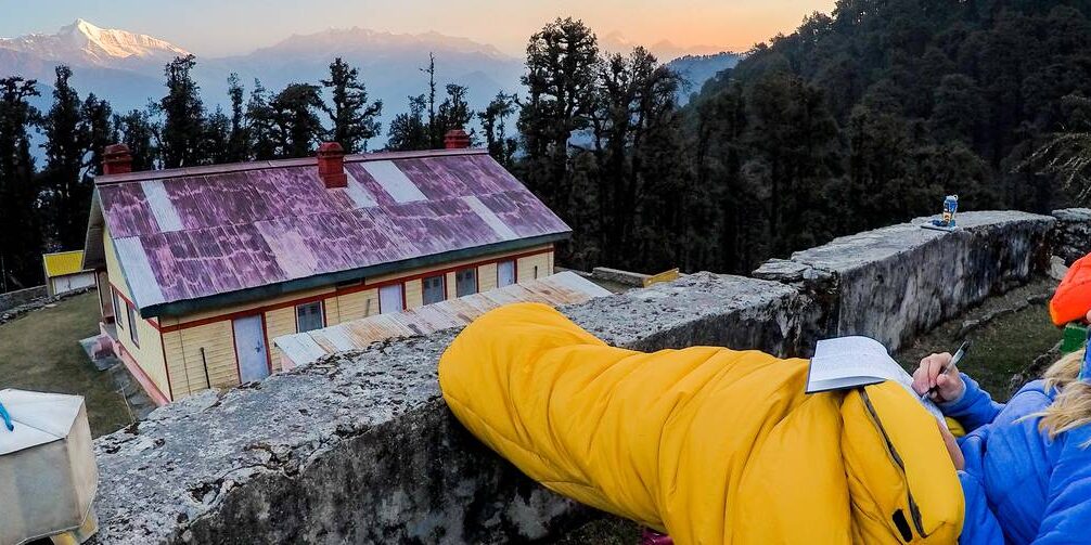 A student journals in their sleeping bag at sunset while looking out at India's Kumaon Himalaya.