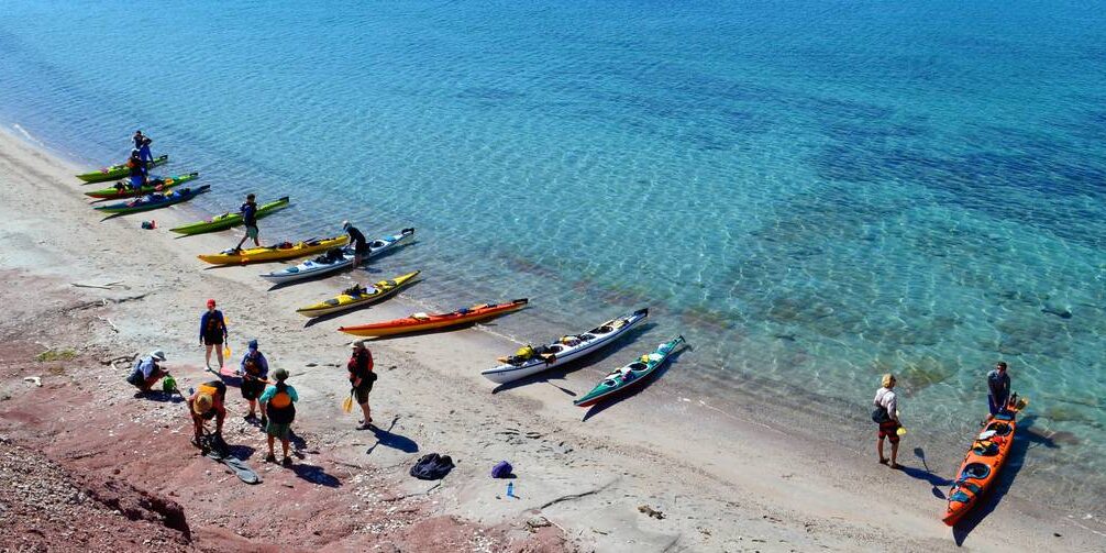 Students loading up their sea kayaks on shore next to the stunning aqua waters of the Sea of Cortez in Baja California, Mexico.