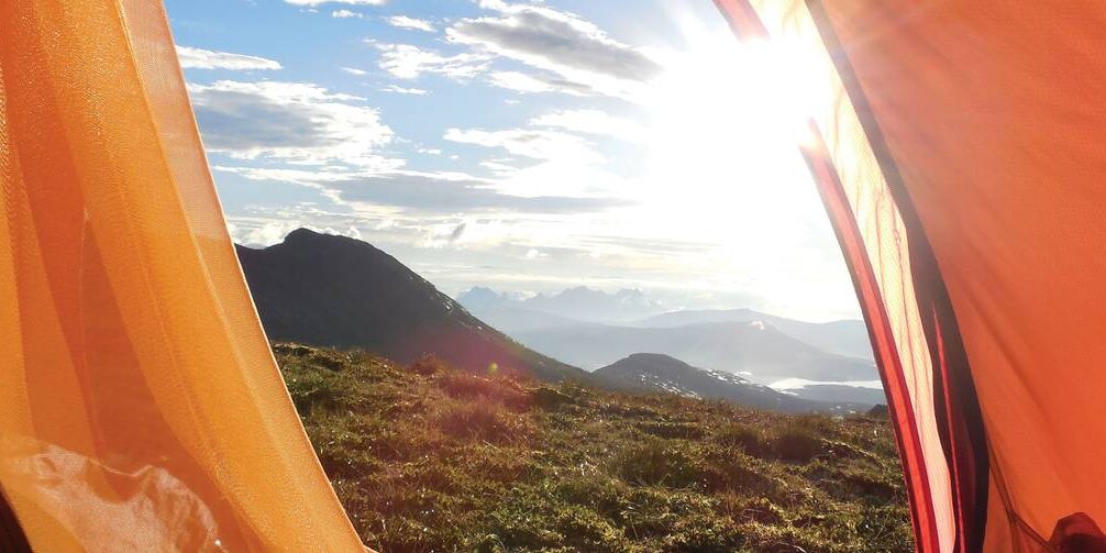 The view of a sunrise while peeking out of the entrance to a tent.